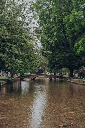 Bourton-on-the-Water, UK - July 12 2020: Woman walking over a small stone foot bridge over the River Windrush in Bourton-on-the-Water, a famous village in rural Cotswolds area of England.のeditorial素材