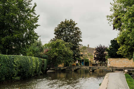 Bourton-on-the-Water, UK - July 12 2020: Couple with a dog walking over a small stone foot bridge over the River Windrush in Bourton-on-the-Water, a famous village in rural Cotswolds area of England.のeditorial素材