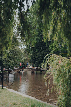Bourton-on-the-Water, UK - July 10, 2020: People walking over a stone foot bridge over the River Windrush in Bourton-on-the-Water, a famous village in rural Cotswolds area of England. Selective focus.のeditorial素材