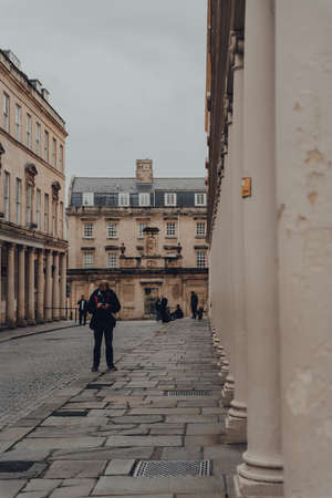 Bath, UK - October 04, 2020: Man in face mask using phone standing on Bath street in Bath, the largest city in the county of Somerset known for and named after its Roman-built baths. Selective focusのeditorial素材