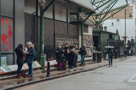 London, UK - November 19, 2020: People standing eating take away food outside Borough Market, one of the largest and oldest food markets in London, as the restrictions on eating indoor are in place.のeditorial素材