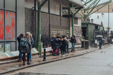 London, UK - November 19, 2020: People standing eating take away food outside Borough Market, one of the largest and oldest food markets in London, as the restrictions on eating indoor are in place.のeditorial素材