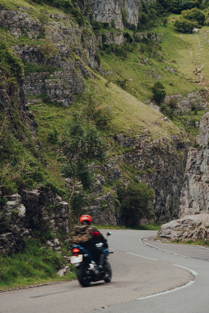 Cheddar Gorge, UK - July 26, 2020: Road going through Cheddar Gorge limestone gorge in the Mendip Hills, near the village of Cheddar, Somerset. Biker riding through, motion blur.のeditorial素材