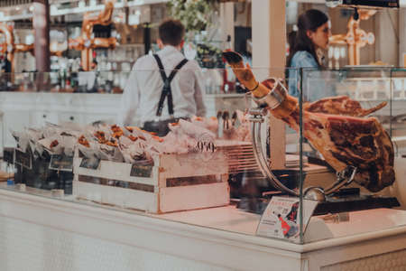 Seville, Spain - January 19, 2020: Serrano ham leg at charcuterie stand inside Lonja del Barranco, gourmet marked housed in a 19th-century building created as a fish market.のeditorial素材