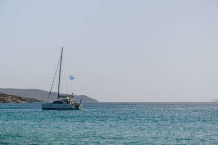 Unidentifiable yacht with a Greek flag in the turquoise water off the coast of Mykonos, Greece, on a sunny summer day.の写真素材