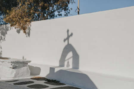 Shadow from the cross and bell on top of a church falling on a whitewash wall in Ana Mera, Mykonos, Greece.の写真素材