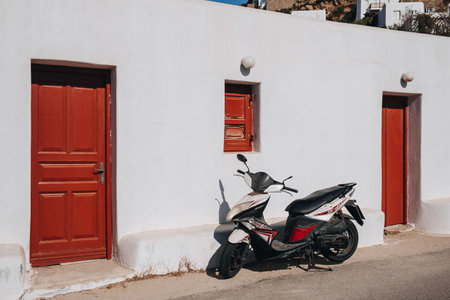 Agios Ioannis, Greece - September 24, 2019: Motorbike parked by a typical whitewashed house with red doors and windows on the Greek island of Mykonos, a popular travel destination in Europe.のeditorial素材