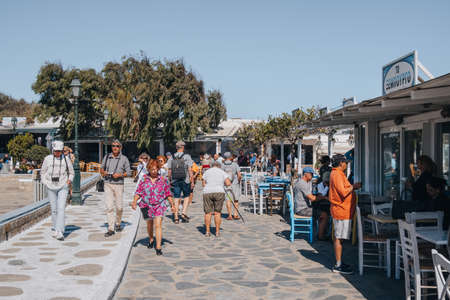 Ana Mera, Greece - September 24, 2019: People walking past the outdoor tables of a restaurant in Ana Mera, a town on Mykonos Island famous for its monasteries, on a sunny day.のeditorial素材