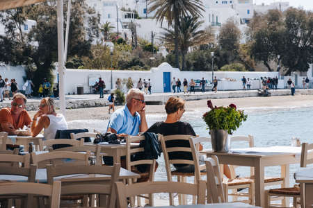 Mykonos Town, Greece - September 24, 2019: People relaxing at the outdoor tables of a restaurant by the water in Hora (also known as Mykonos Town), capital of the Mykonos island.のeditorial素材