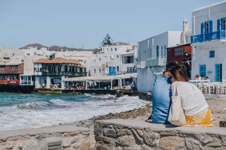 Mykonos Town, Greece - September 24, 2019: Young Asian couple relaxing and enjoying the view by the water in Little Venice area of Hora (also known as Mykonos Town), capital of the Mykonos island.のeditorial素材