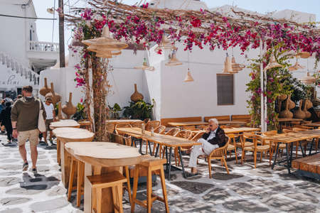 Mykonos Town, Greece - September 24, 2019: Senior man taking on phone, relaxing at the outdoor tables of a restaurant in Hora (also known as Mykonos Town), capital of the Mykonos island.のeditorial素材