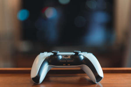 London, UK - May 25, 2021: One white Playstation 5 (PS5) controller on the table, tv on background,...