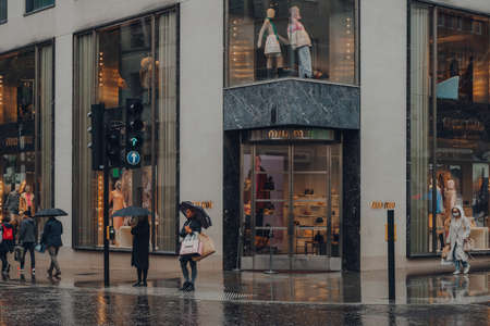 London, UK - October 02, 2021: Miu Miu store on Bond Street, one of the most famous streets for luxury shopping in London, people with umbrellas in front.のeditorial素材