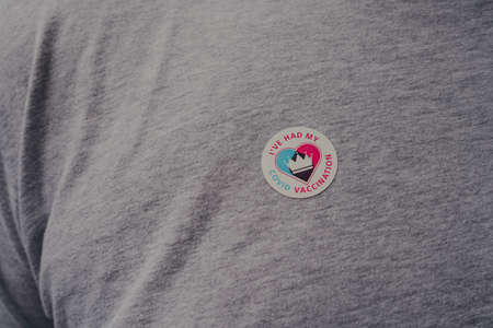 London, UK - December 17, 2021: Close up of NHS Vaccination programme I've Had My Covid Vaccine sticker on a grey t-shirt, received after successful Covid-19 vaccination, selective focus.のeditorial素材