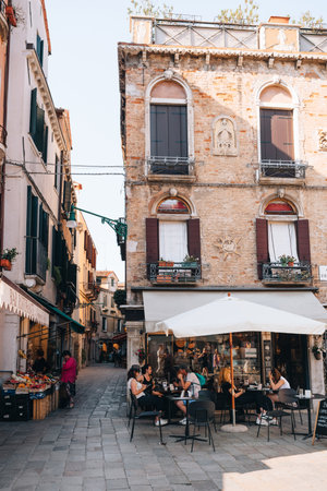 Venice, Italy - May 21, 2022: People at the outdoor tables of a restaurant on a narrow street in Venice, capital of Veneto region and a famous travel destination.のeditorial素材