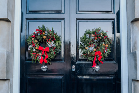 Traditional green, red and white Christmas wreaths on a double black front door of an English house in London, UK.の写真素材