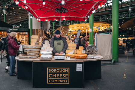 London, UK - January 27, 2023: Man working at a Borough Cheese Company stall in Borough Market, one of the largest and oldest food markets in London.のeditorial素材