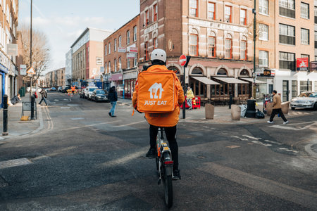 London, UK - February 09, 2023: Just Eat delivery driver on a street in East London. Just Eat is a company that enables food to be delivered from restaurants that do not offer delivery.のeditorial素材