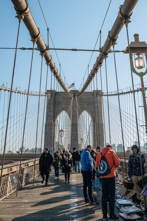 New York, USA - November 21, 2022: People buying souvenirs from sellers on Brooklyn Bridge, a famous hybrid cable-stayed-suspension bridge in New York City, on a sunny winter day.のeditorial素材