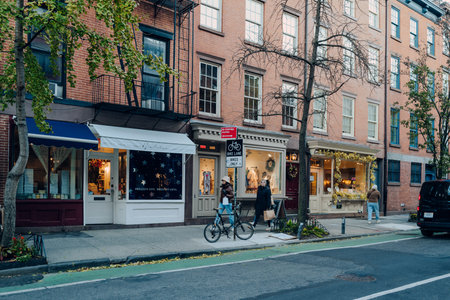 New York, USA - November 21, 2022: Row of shops on a street in West Village, a charming area of Manhattan famous for its shops and restaurants, women walking past.のeditorial素材
