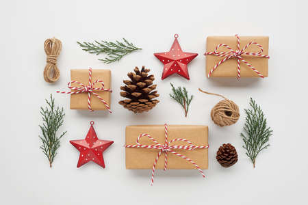 Christmas composition with gift boxes wrapped in craft paper, pine cones, conifer branches, decorative toys on white background. Flat lay, top view.の写真素材