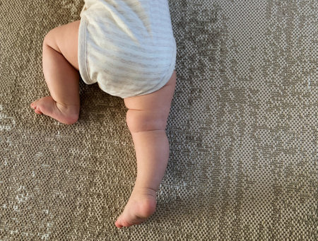 Cute little baby feet on the floor. A child in a light striped bodysuit is crawlingの写真素材