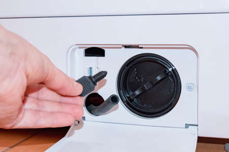 Washing machine with an open filter cover, hand holds part, key, partの写真素材