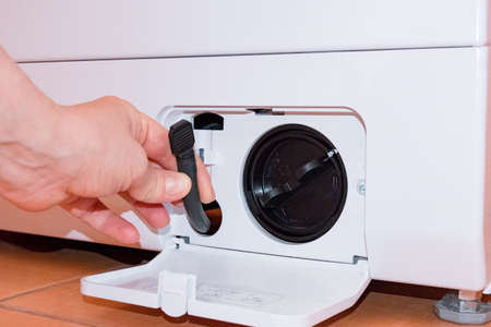 Washing machine with an open filter cover, hand holds part, key, partの写真素材