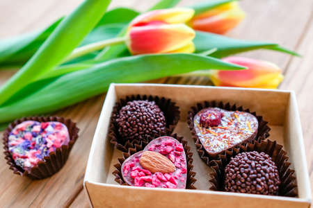 Handmade chocolates in a box next to tulnans for a holiday, wooden backgroundの写真素材