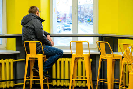 A man sits facing the window, his face is not visible. Yellow cafe interior. lonely manのeditorial素材