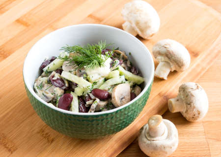 Salad with cucumbers, beans and mayonnaise. The dish is decorated with dill. Mushrooms are on the backgroundの写真素材