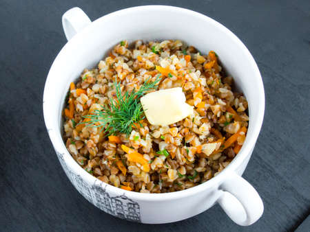 Porridge with vegetables in a white bowl. Garnished with a sprig of parsley. Buckwheat with onions and carrotsの写真素材