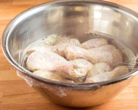 Chicken drumstick soaked in mayonnaise. A bowl of chicken in the sauce is covered with a transparent kitchen bagの写真素材