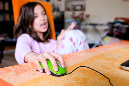 Focus - computer mouse, hand. The child is sitting on a chair, studying at the computer. Discontent. Study at home. Blurred backgroundの写真素材