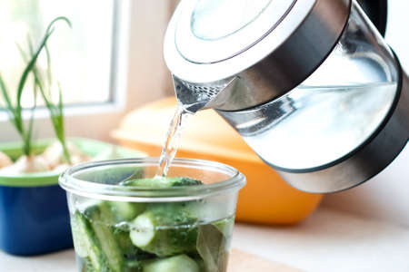 Pour water from a kettle into a jar of cucumbers. Preparation for the winterの写真素材