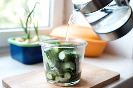 Pour water from a kettle into a jar of cucumbers. Preparation for the winterの写真素材