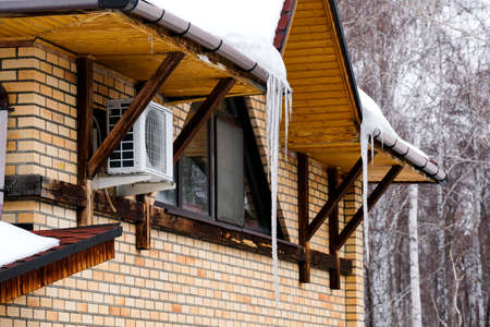 Large icicles hang under the roof of a private house. Spring drops.