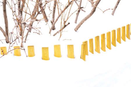 Wooden yellow low fence in the snow. Lilac bushes are visible.の写真素材