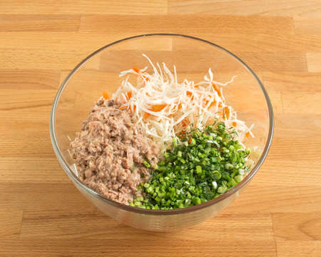 Ingredients in a transparent fish salad bowl. Canned food, chopped green onions, fresh cabbage.の写真素材