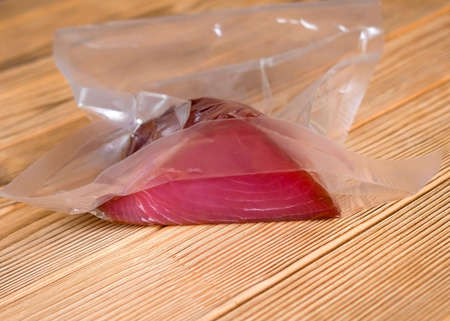A piece of tuna in a vacuum package on a wooden background. No people, blurred background.の写真素材