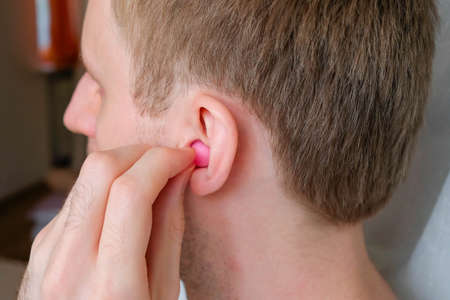A man puts a earplug in his ear. Wax pink ear plug.の写真素材