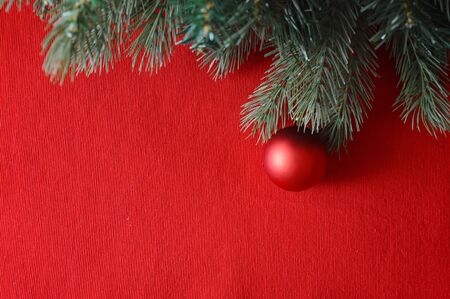 Spruce green branches on a red background and red ball, Christmas toy. Happy New year and merry Christmas. Postcard for a holiday.の写真素材