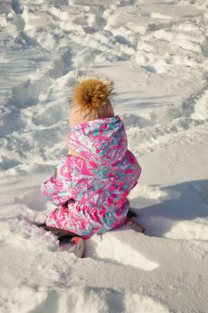 A little beautiful girl is playing in the snow-white snow with snowballs in winter. Happy childhood....