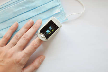 Pulse oximeter on the finger and a medical mask on a white background. A device for measuring saturation. . Viral infection.の写真素材