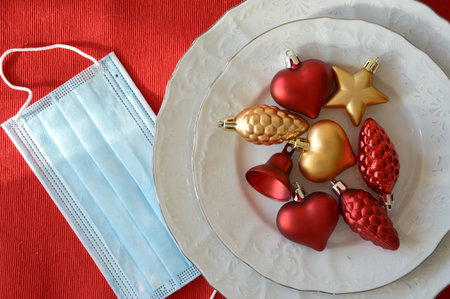 Christmas table. white plates with toys, a knife and fork on a red background and a medical...