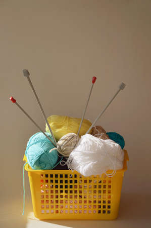 knitting day. multicolored skeins of woolen threads and knitting needles in a yellow basket. handiwork.の写真素材