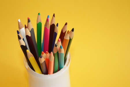 colored pencils in a white glass on a yellow background. stationery, school supplies.の写真素材