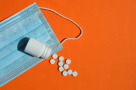 Pills for the treatment of human diseases. medicines in a white jar. medicines on an orange background. virus, covid and protective mask.の写真素材