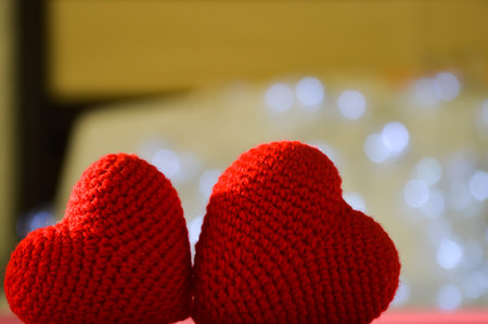 Two red knitted hearts on a red background with bokeh