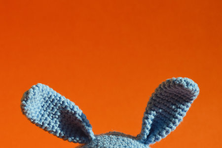 Blue knitted bunny ears on an orange background. close-upの写真素材